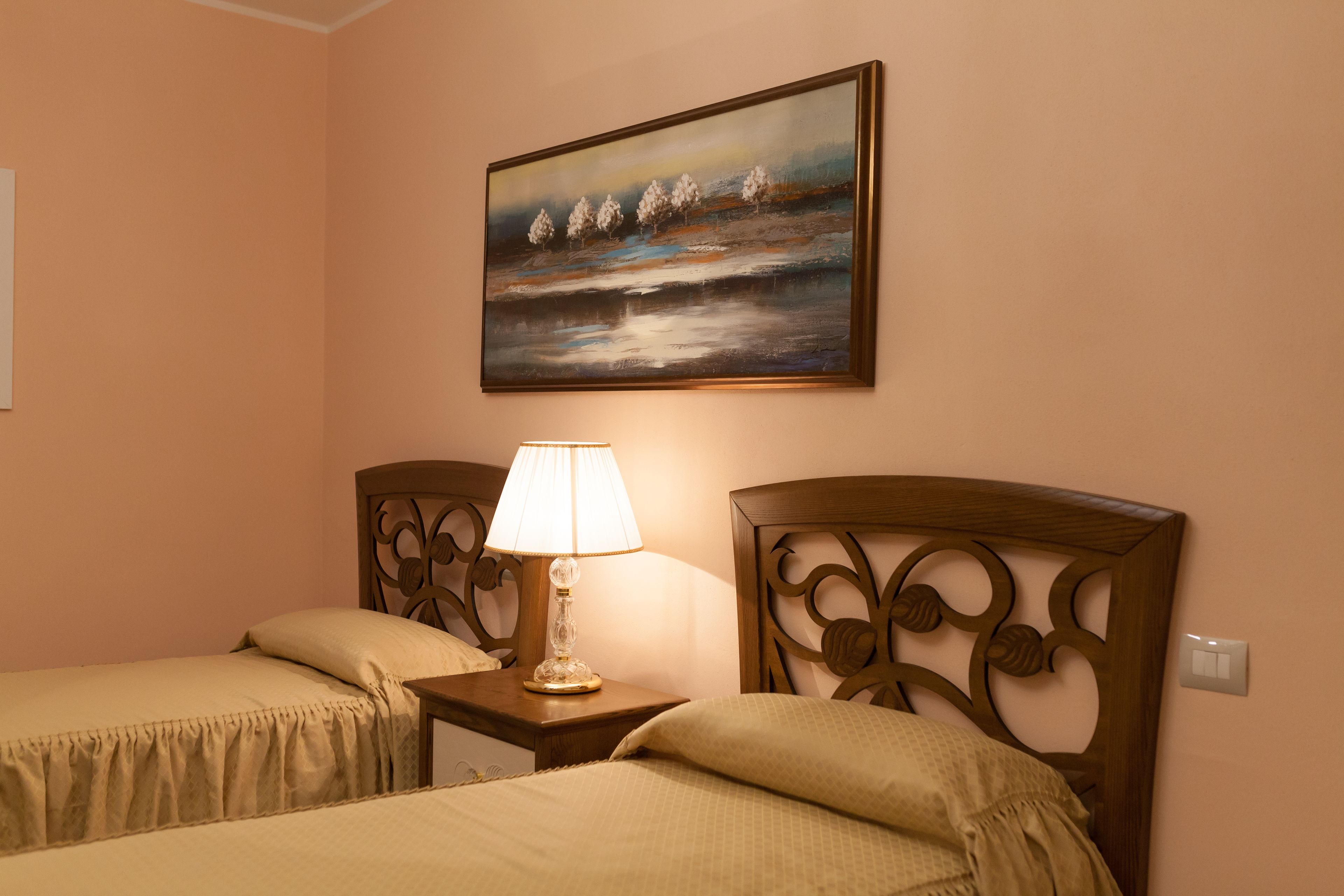 A hotel room with two single beds, a nightstand with a lamp, and a painting on the wall.