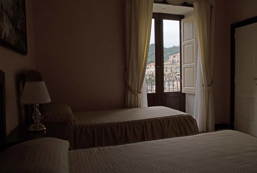Una habitación de hotel con dos camas, una ventana con cortinas y una lámpara en una mesita de noche.