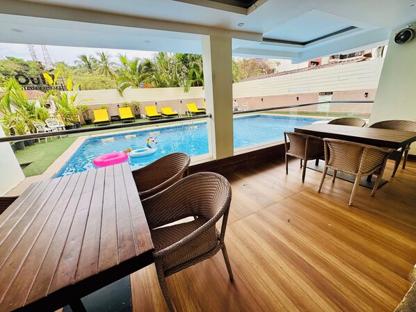 Un espace aménagé au bord de la piscine, avec des fauteuils en osier, une table en bois et une vue sur la piscine.