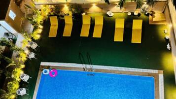 Ein Pool auf dem Dach mit glatter, blauer Wasseroberfläche, umgeben von gelben Liegestühlen und Topfpflanzen.