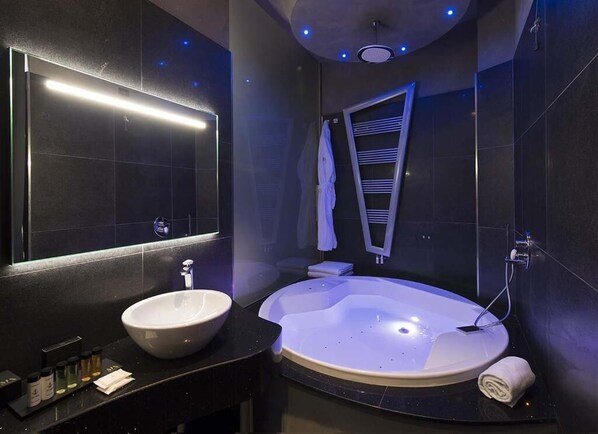 A modern bathroom with a large mirror, a round bathtub, a sink, and a towel rack.