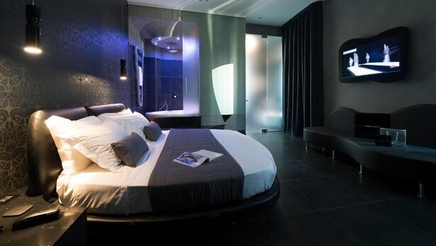 A modern hotel room with a curved bed, a flat-screen TV mounted on the wall, and a seating area with a coffee table. - Gatto Bianco Mia Aparthotel (Milan)