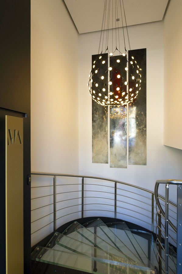 Interior moderno com escada de vidro, guarda-corpo metálico e luminária pendente singular.
