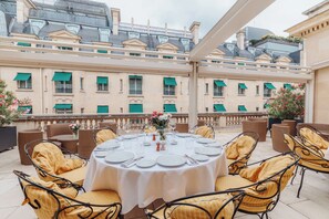 A round table set for dining with wicker chairs, a balcony with a view of buildings, and a railing. - Majestic Apartments Champs Elysées (Paris)