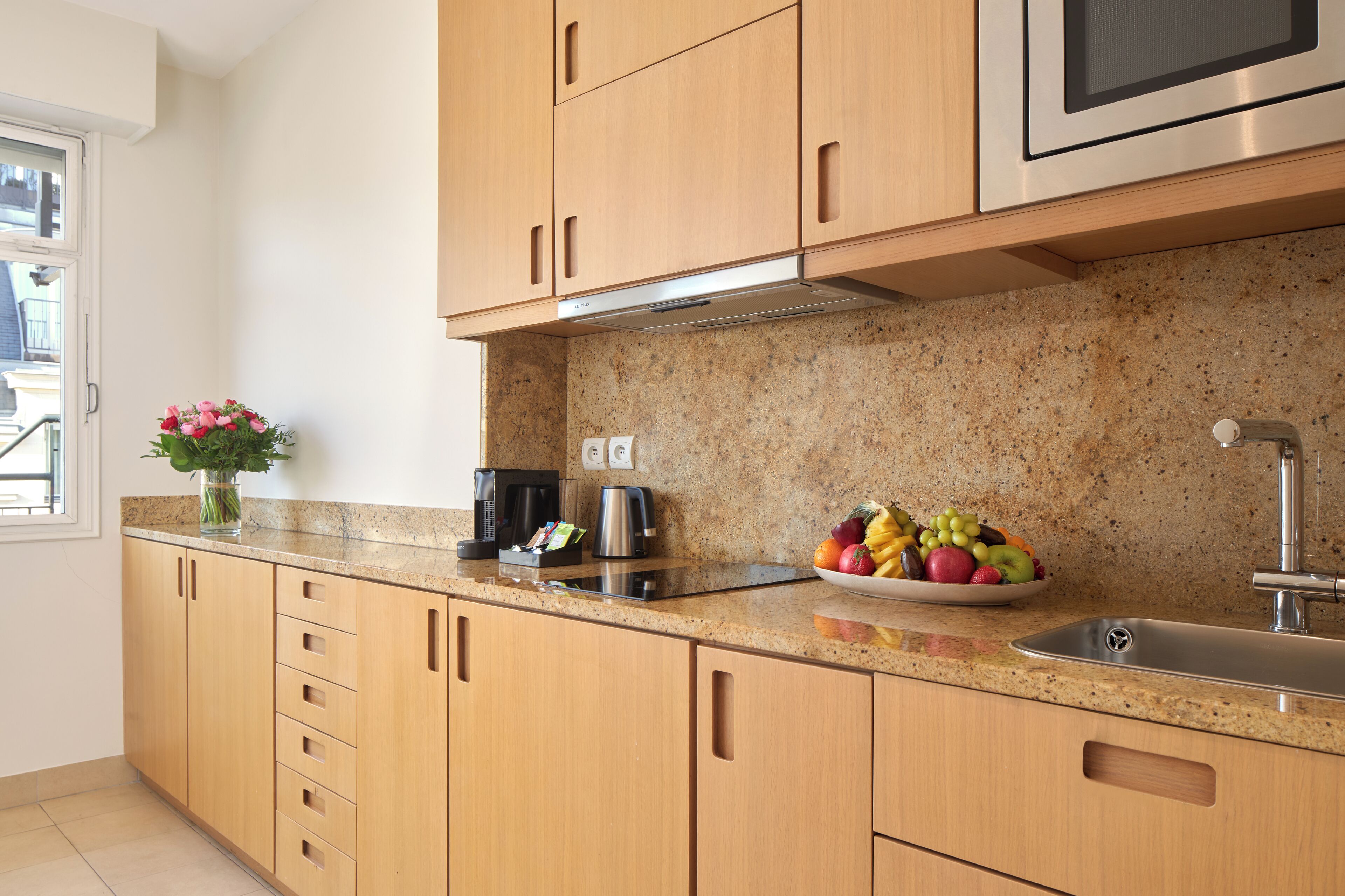 A kitchen with wooden cabinets, a granite countertop, a stainless steel sink, and a fruit bowl.