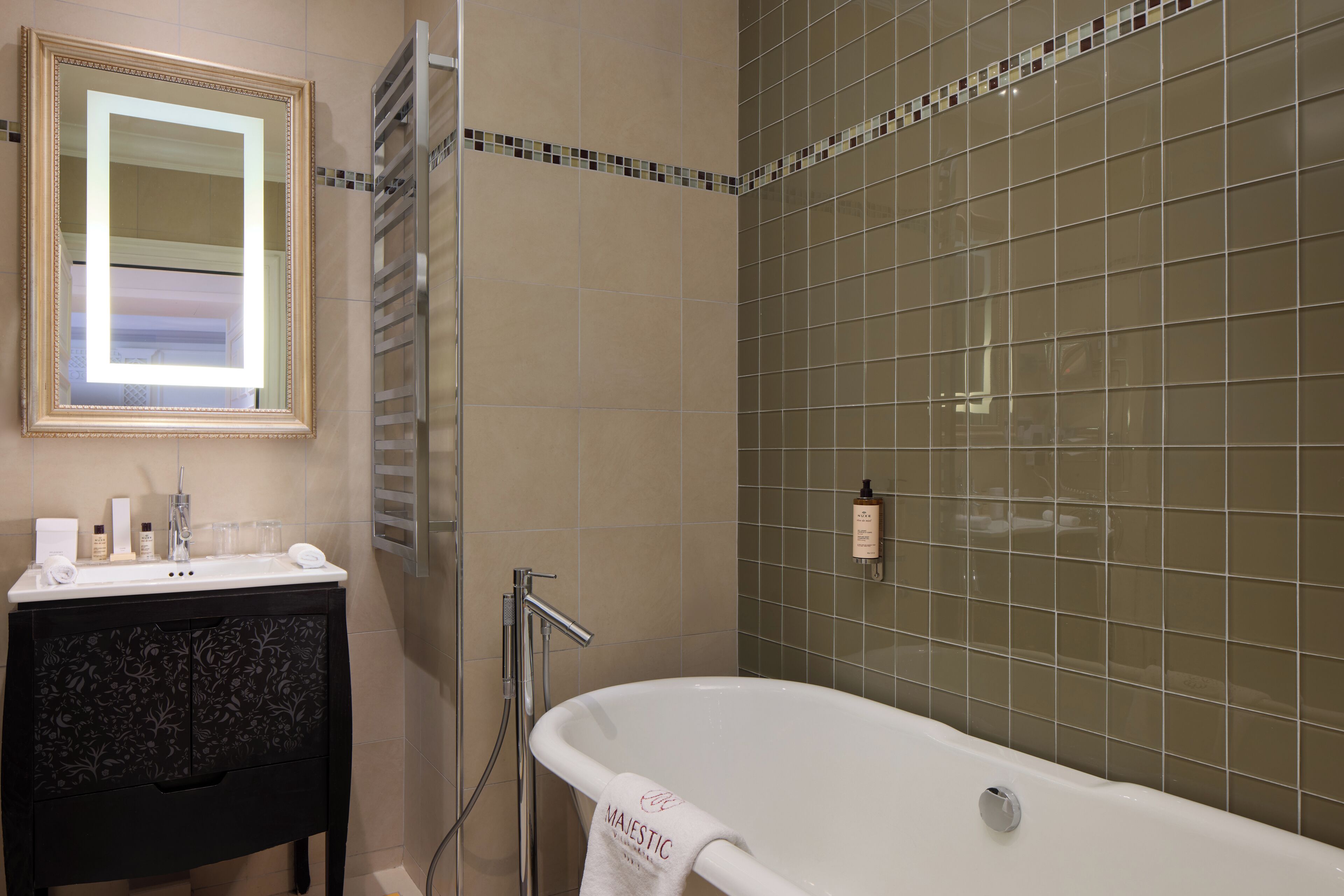 A bathroom with a white bathtub, a vanity with a mirror, and a tiled shower wall.