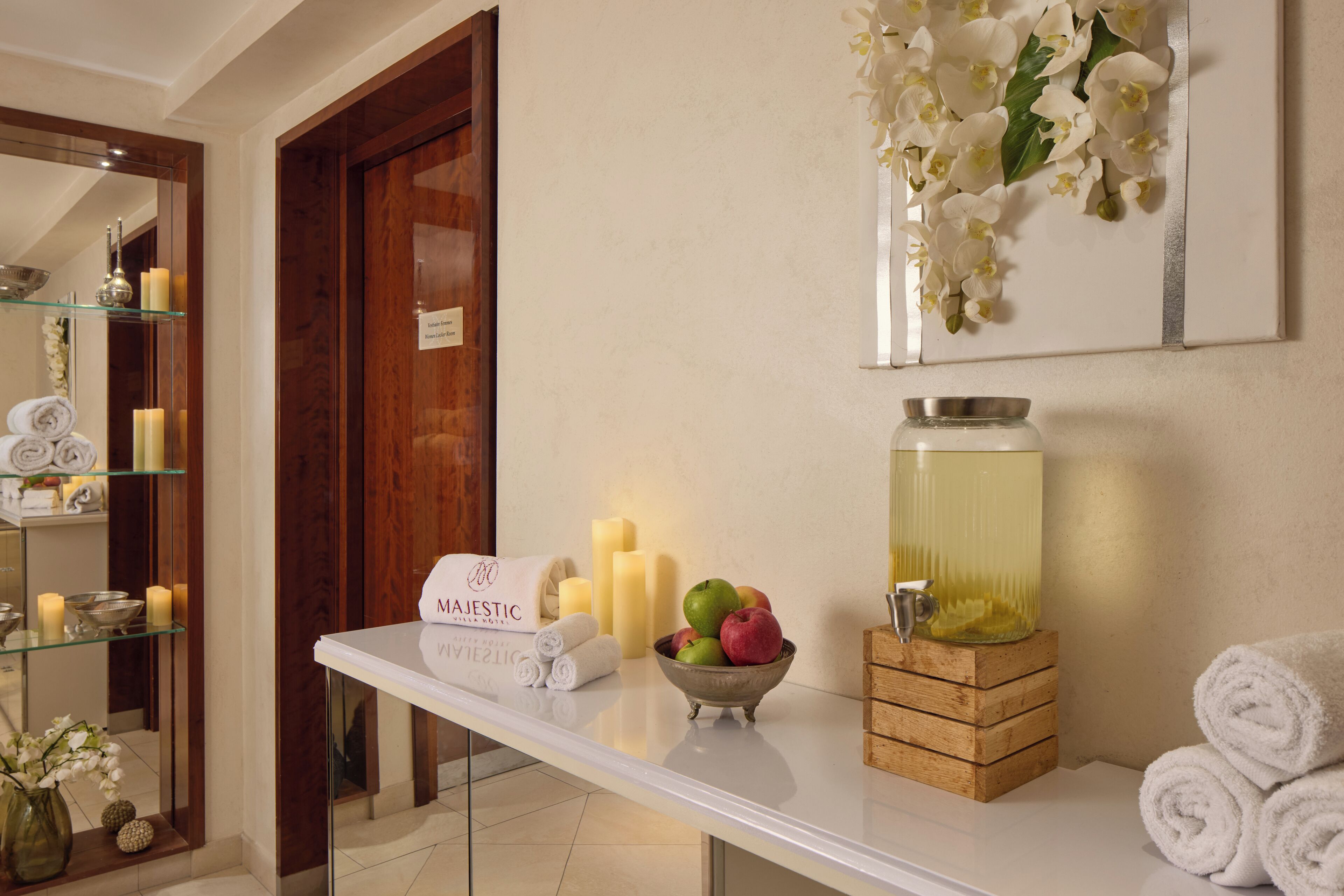 A spa area with a reception desk, a mirror, a bowl of fruit, candles, and a water dispenser.