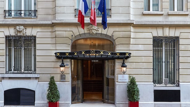 A grand building with ornate architectural details, a prominent entrance with a canopy, and flags of France and the European Union.