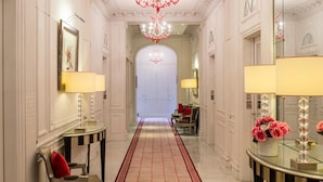 A grand hallway with a red carpet, ornate white walls, and a large chandelier.