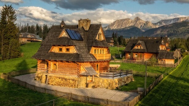 A traditional wooden house with a stone foundation, a wooden deck, and a mountain backdrop. - Willa Giewontka (Koscielisko)