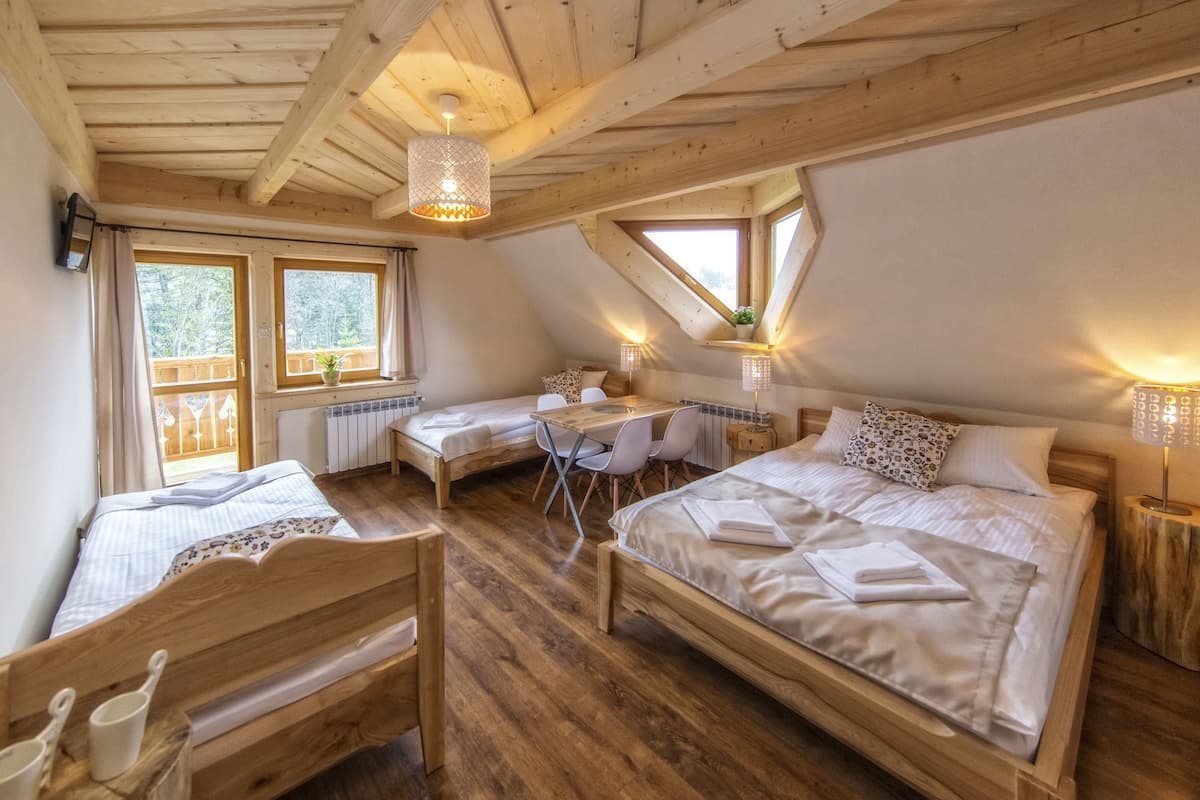 Ein gemütliches Schlafzimmer im Dachgeschoss mit Holzbalken, zwei Betten, einem Schreibtisch und einem Esstisch.