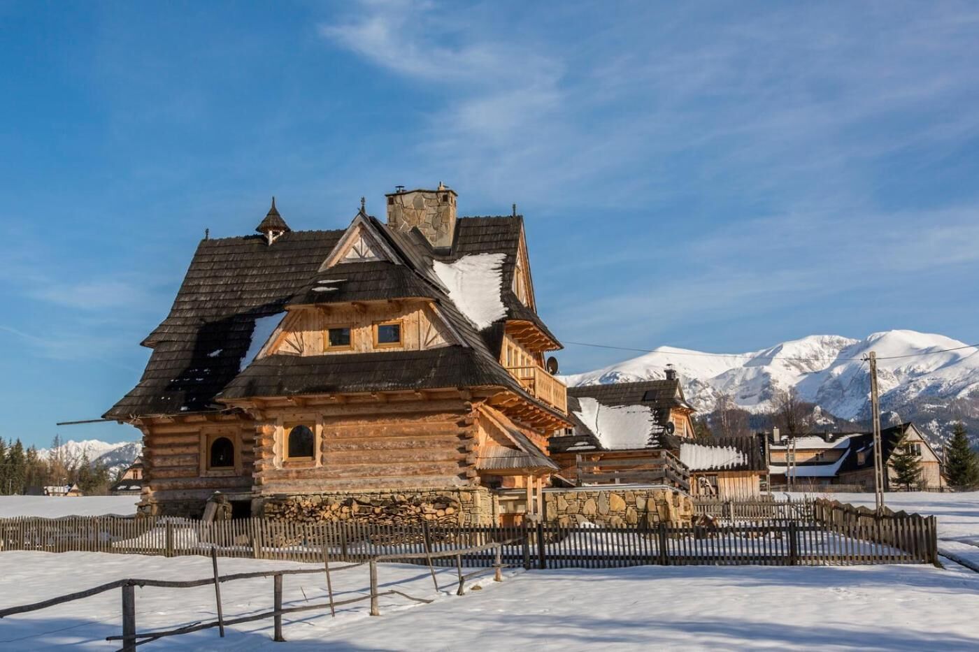 A traditional log cabin with a steeply pitched roof, stone chimney, and wooden balconies.