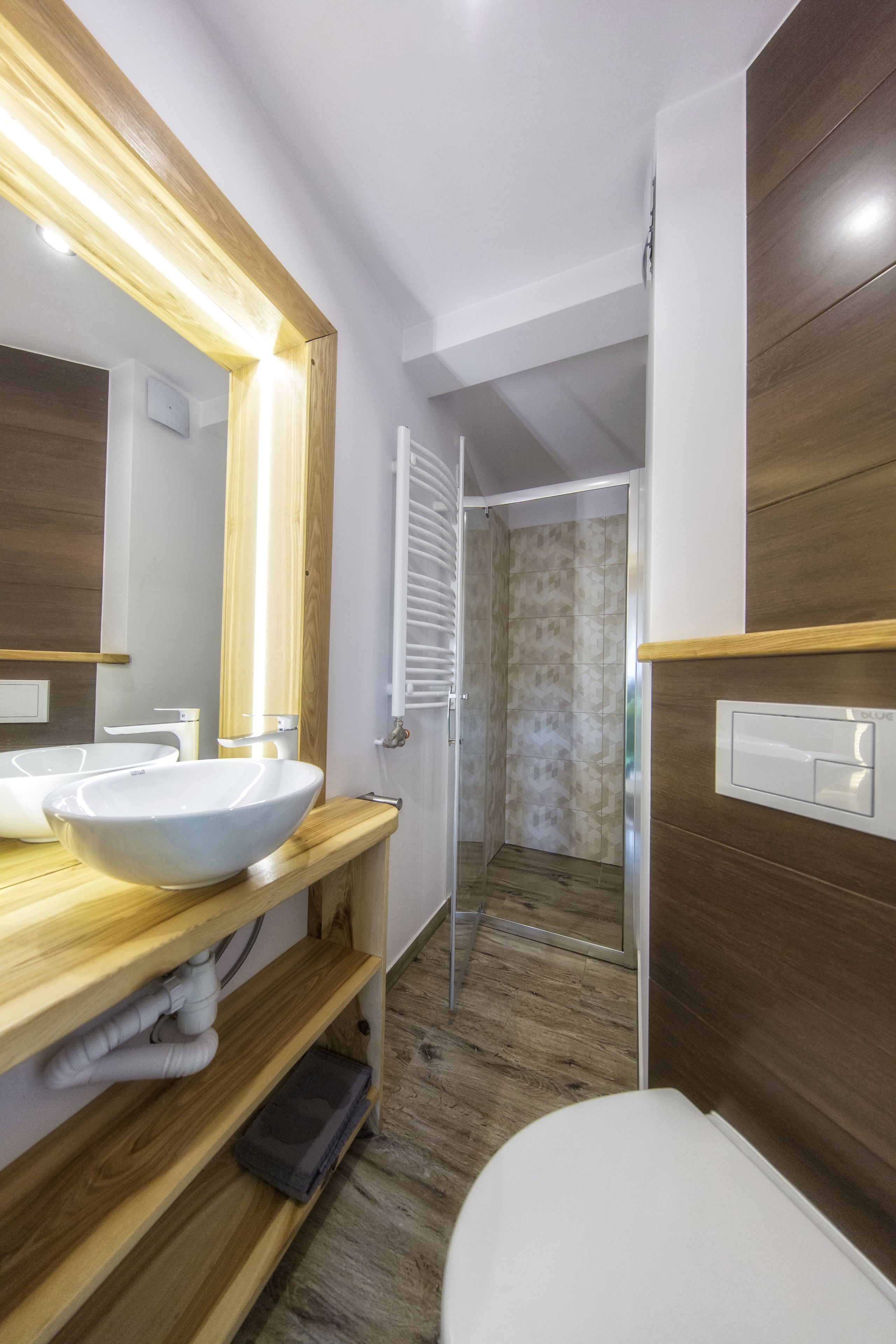 Une salle de bain moderne avec un meuble-lavabo en bois, un grand miroir, un lavabo blanc et un espace douche.