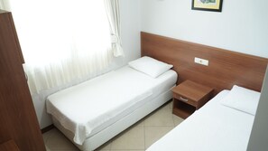 Una cama pequeña y bien hecha, con cabecera de madera y una mesita de noche con un cajón.