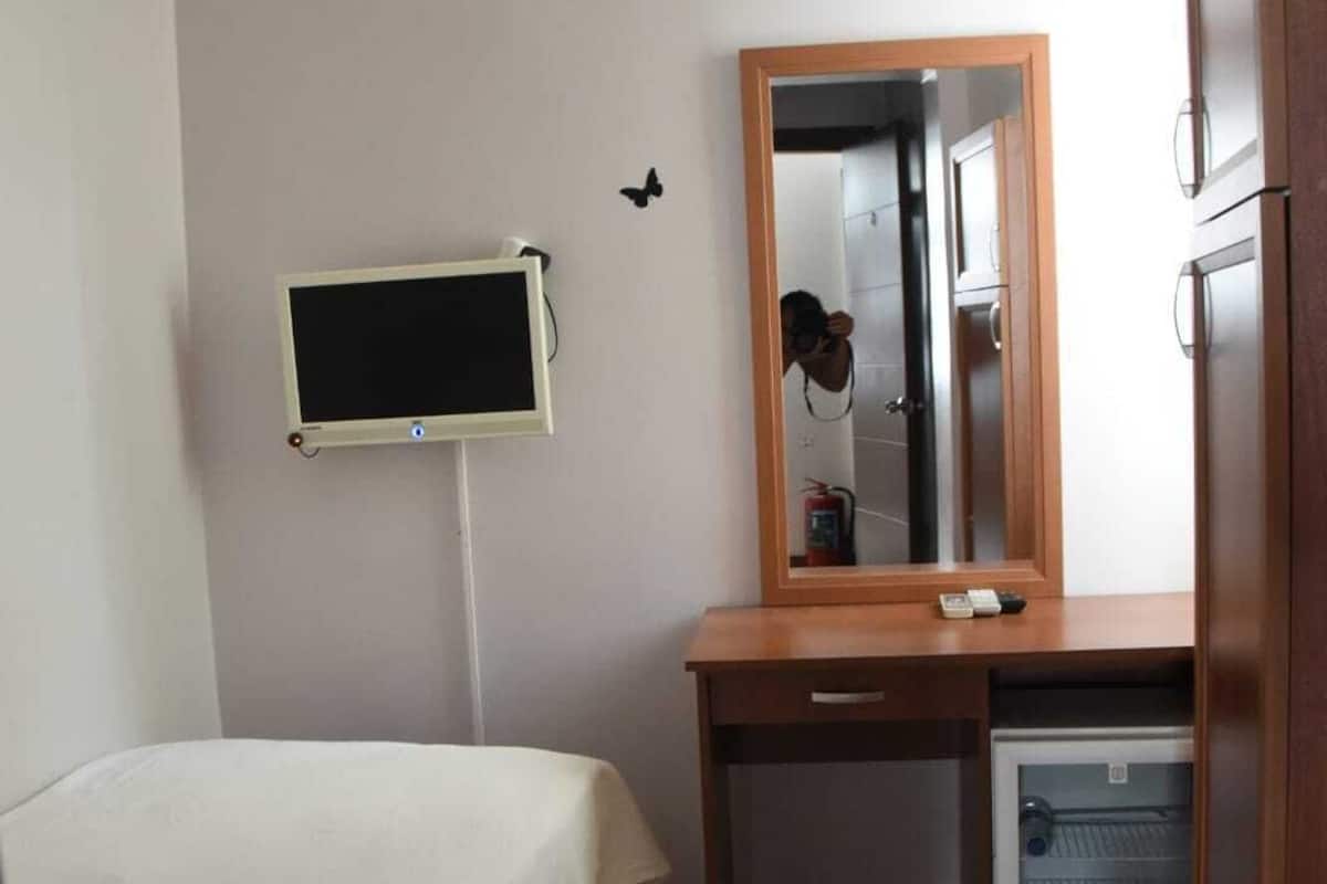 A hotel room with a bed, a desk, a mirror, a television, and a refrigerator.