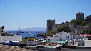 Un pueblo costero con un castillo histórico, barcos en el puerto y edificios modernos.