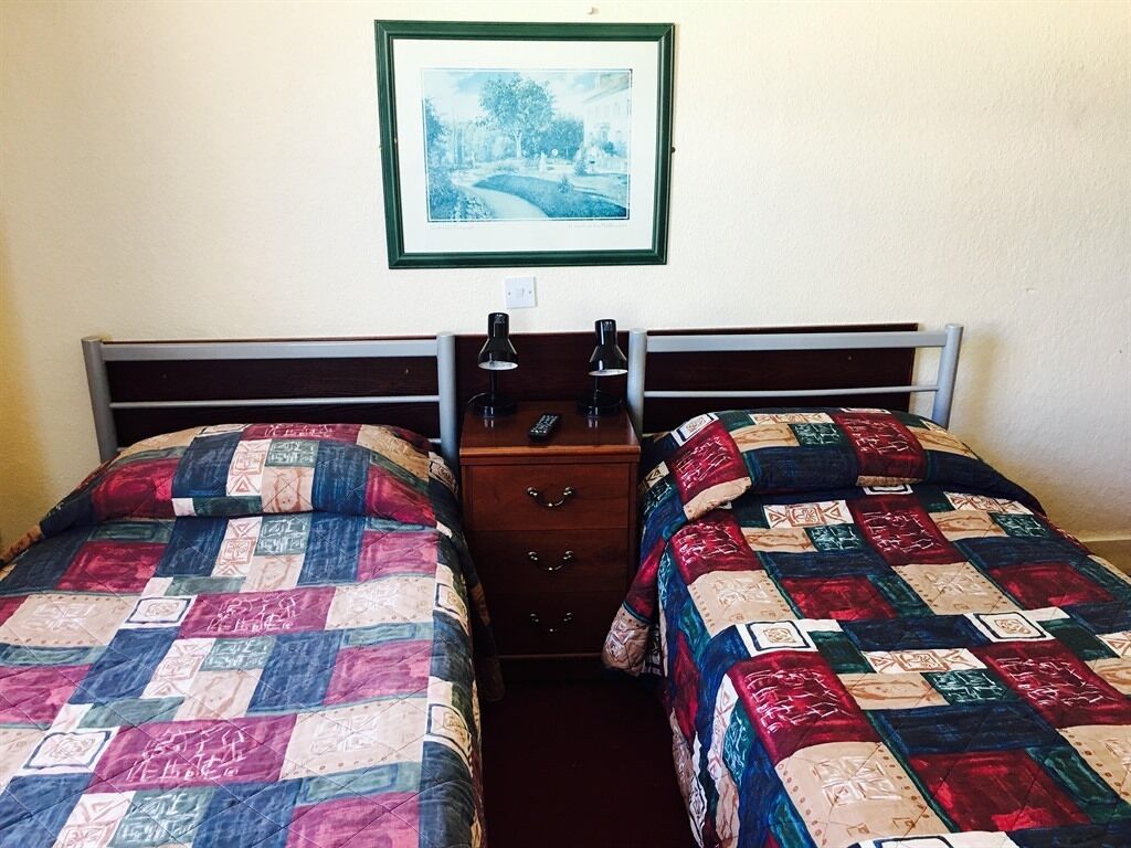 A room with two single beds, a nightstand with a lamp, and a framed picture on the wall.