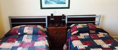 A room with two single beds, a nightstand with a lamp, and a framed picture on the wall.