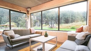 Un salon moderne avec un canapé, une table basse et de grandes fenêtres donnant sur une zone boisée.