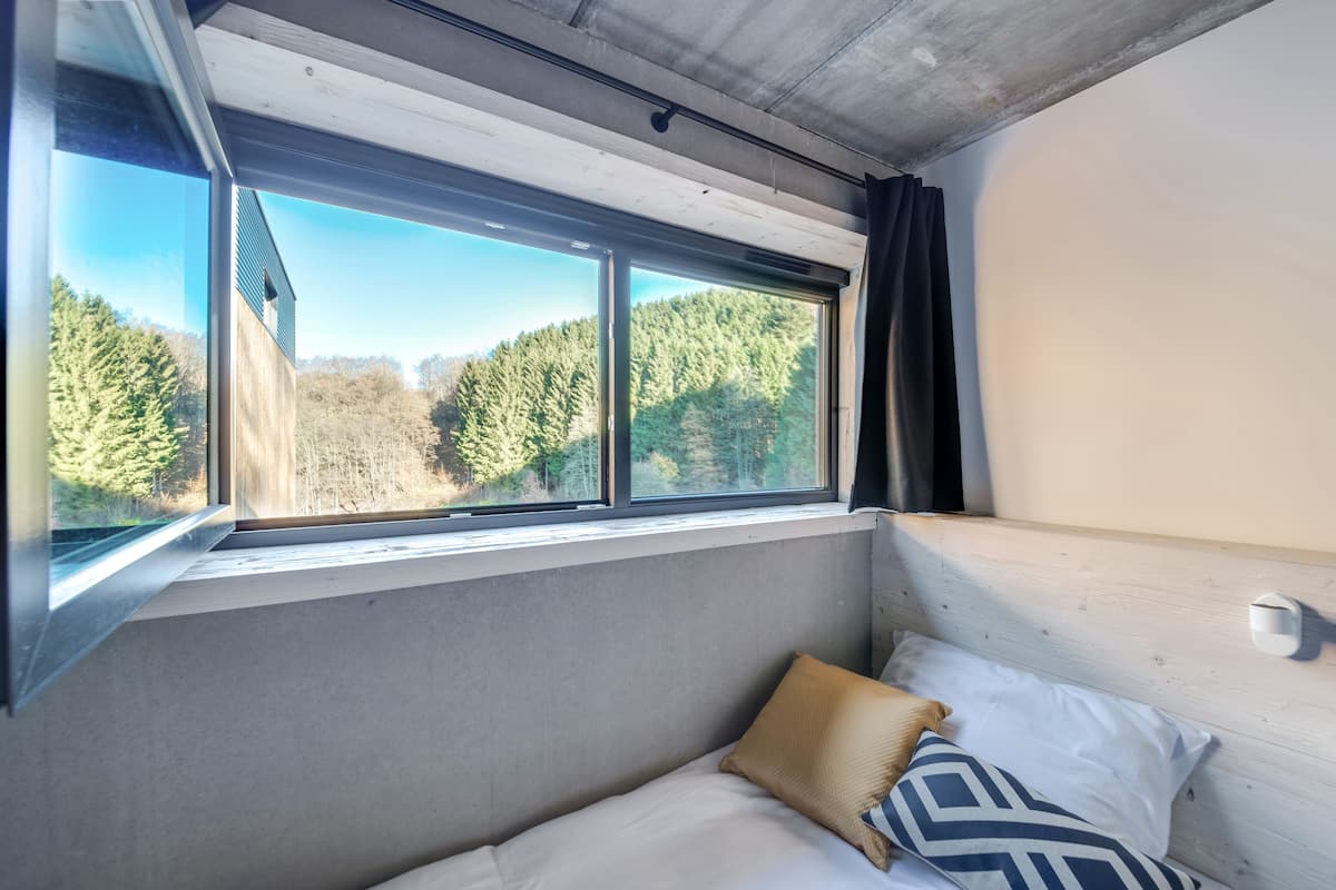 A bunk bed with a window view of a forest.