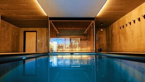 Une piscine intérieure avec des murs et un plafond en bois, une paroi en verre transparent et une porte visible sur le côté gauche.