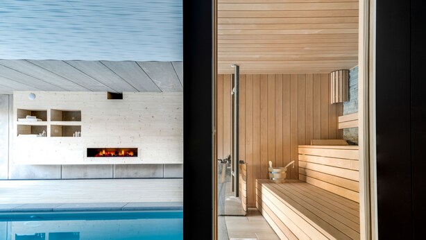 Un espace piscine intérieur moderne, doté d’un sauna en bois et d’une cheminée en pierre.