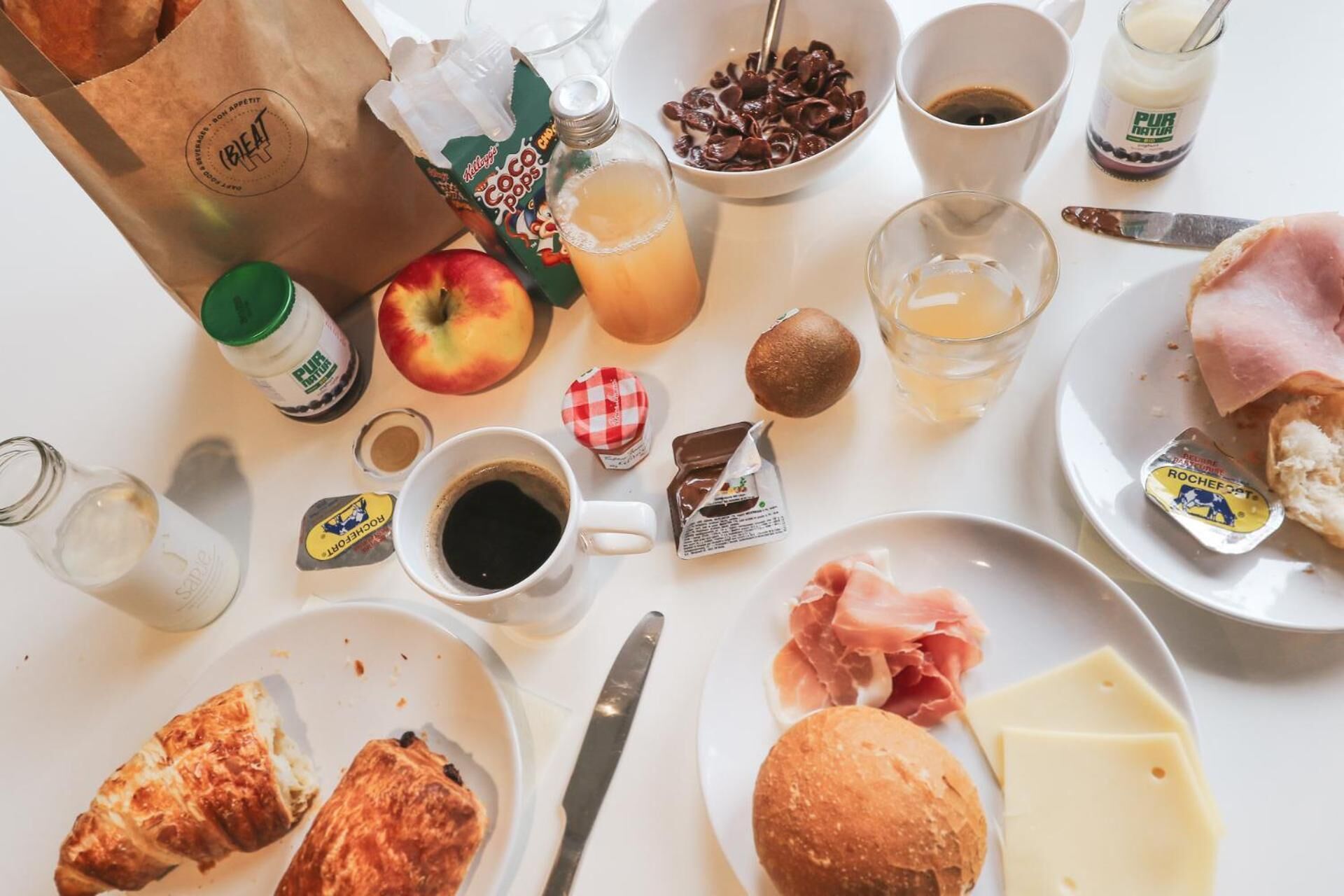 Una mesa de desayuno con diversos alimentos, como pastelería, queso, jamón y bebidas.