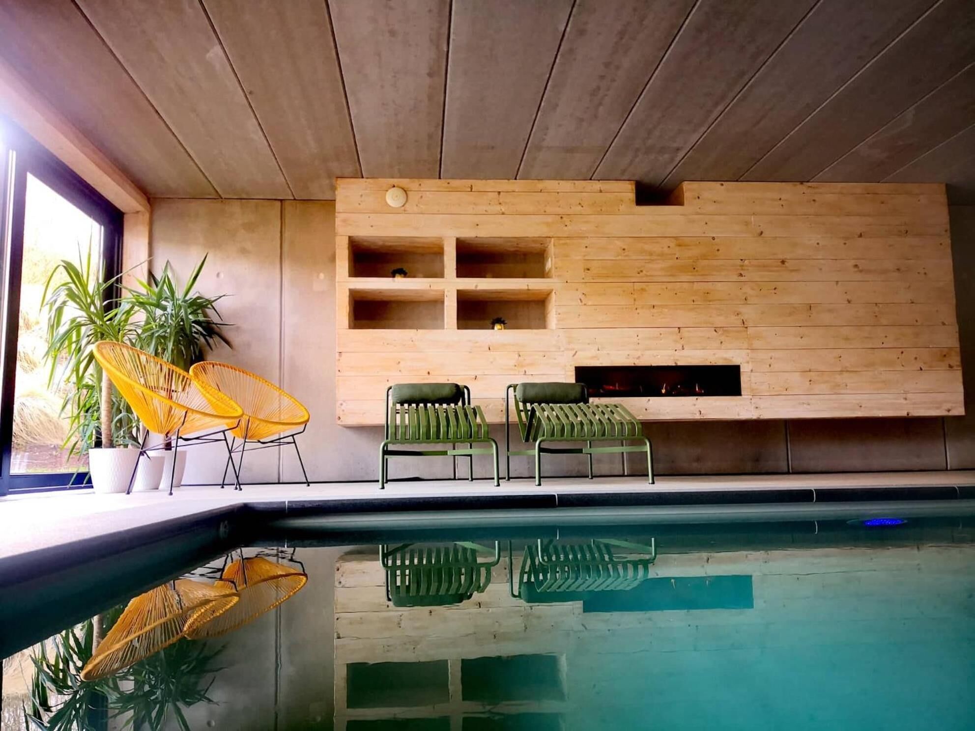 Ein moderner Poolbereich im Innenbereich mit Holzwänden, zwei grünen Sesseln und einem gelben Sessel.