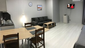 A modern, well-lit room with a dining table, chairs, a sofa, a TV, and a clock on the wall. - ATM Aparts Sofia (Sofia)