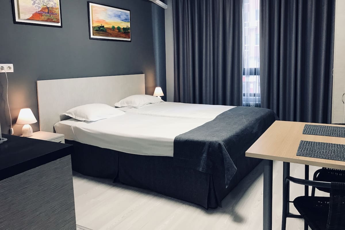 A modern hotel room with a large bed, a desk with a computer, and two paintings on the wall.