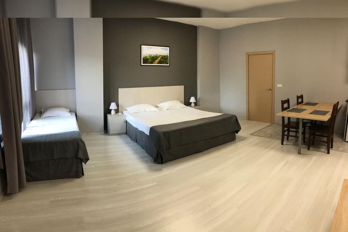 A hotel room with a large bed, a smaller bed, a desk with chairs, and a painting on the wall.