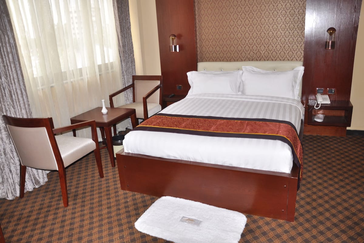 A hotel room with a large bed, a desk, a chair, and a small table.