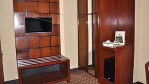 Ein Hotelzimmer mit einer Wandpaneele aus Holz, einem flachbildfernseher, der daran befestigt ist, einer kleinen Holzbank und einem Holzkasten mit Telefon und Taschentuchbox.