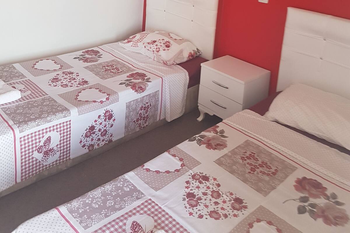 Un dormitorio con dos camas, una mesita de noche y una lámpara fijada a la pared.