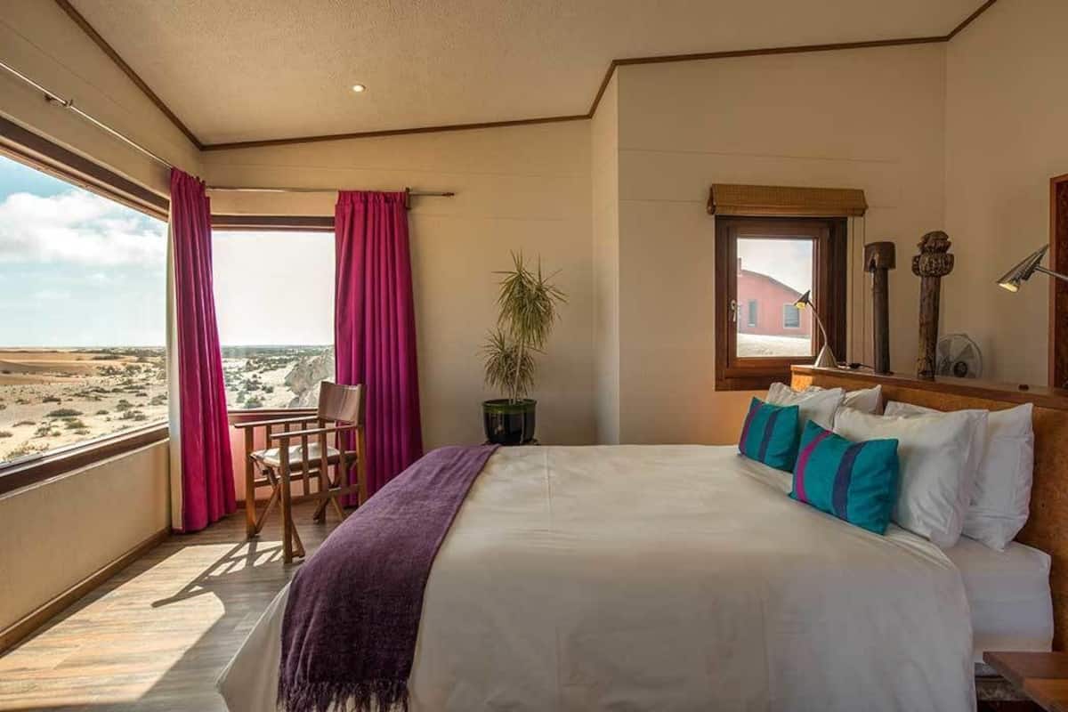 Une chambre avec un grand lit, une vue sur le désert et un balcon équipé d’une chaise.