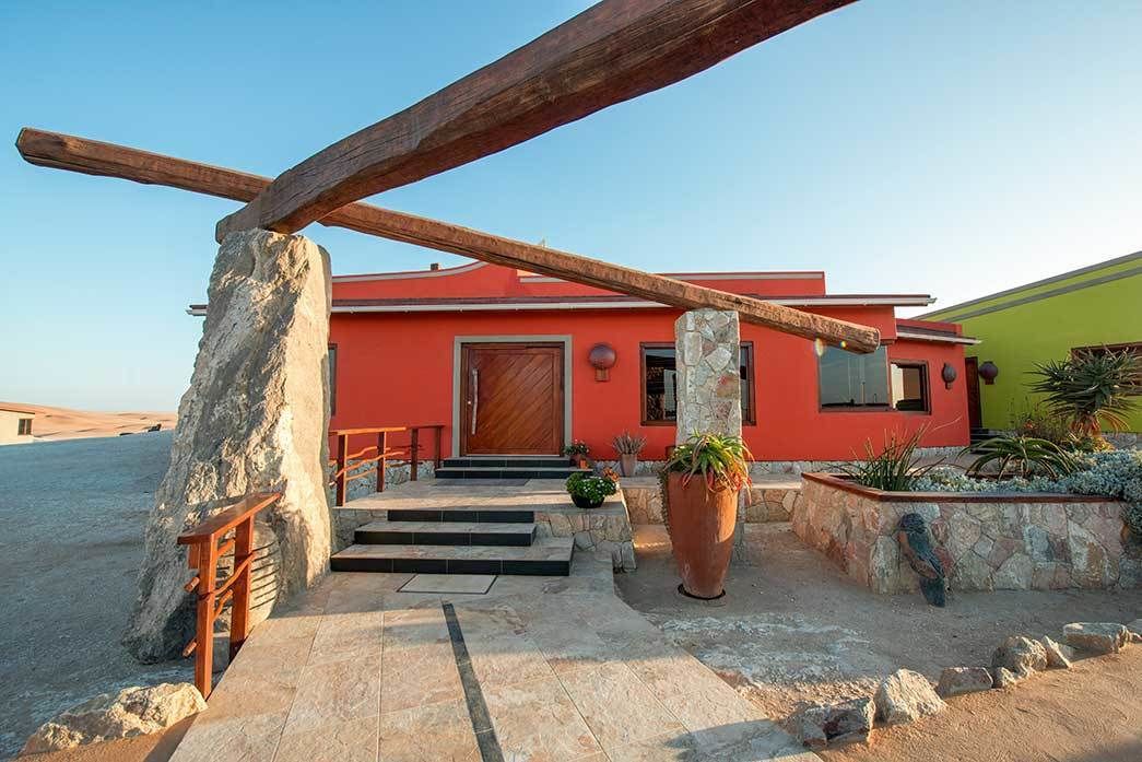 A modern house with a red facade, stone pillars, and a wooden staircase leading to the entrance.