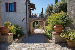 Un sendero de piedra que conduce a un edificio rústico con un puente de madera, plantas en macetas y mesas al aire libre.