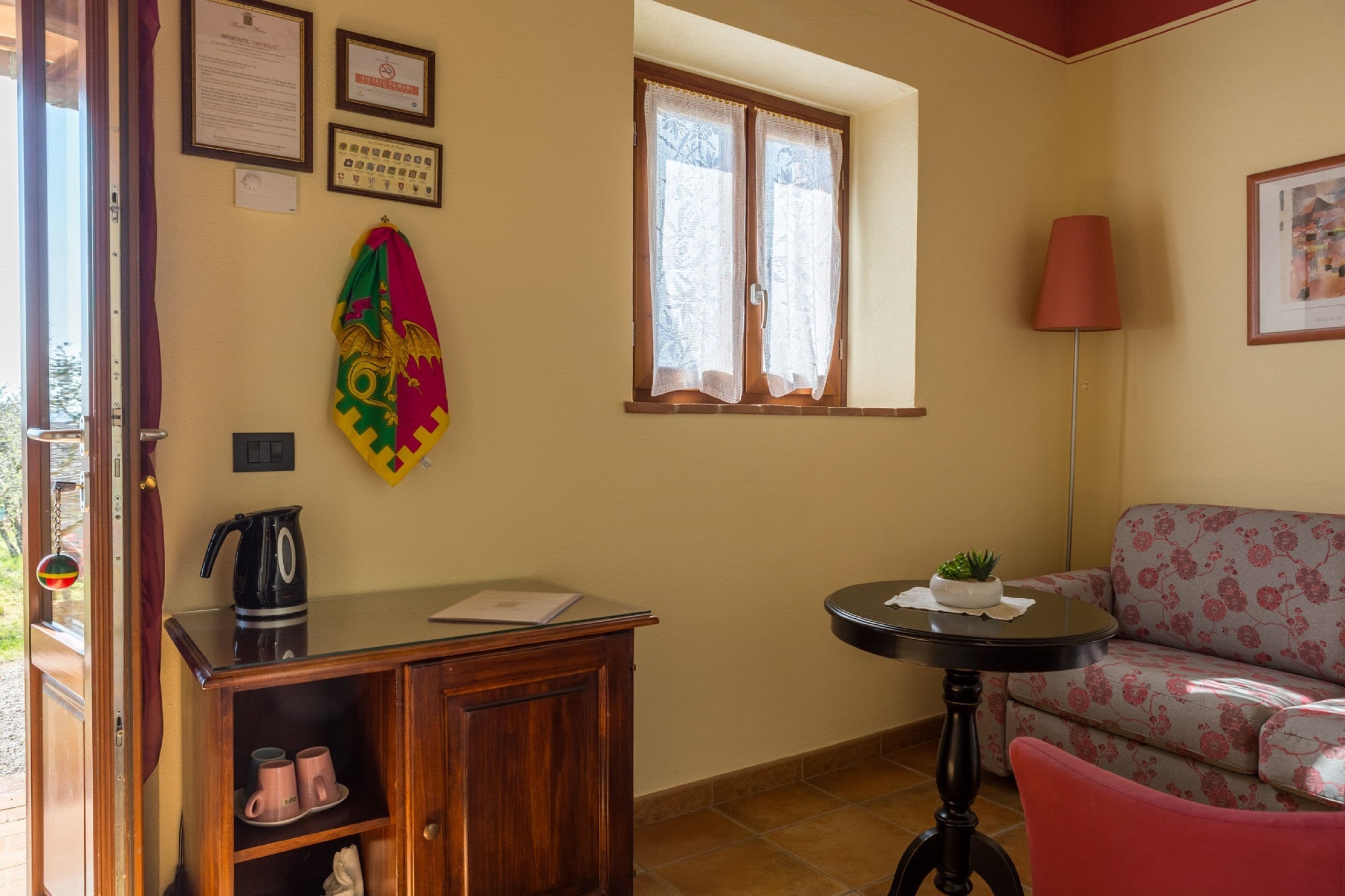 Une pièce avec un bureau en bois, un canapé, une petite table avec une plante et une fenêtre avec des rideaux.