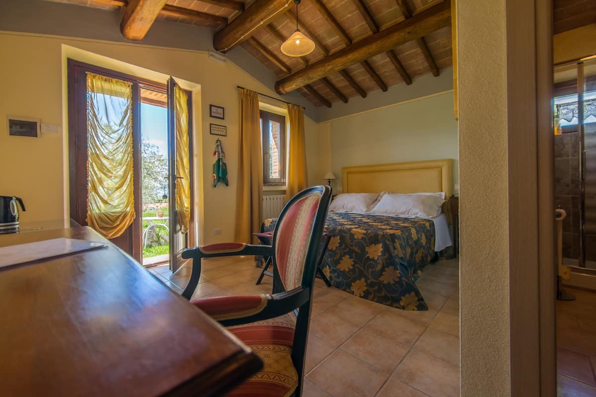 A room with a wooden ceiling, a bed with a floral bedspread, a chair, and a table.