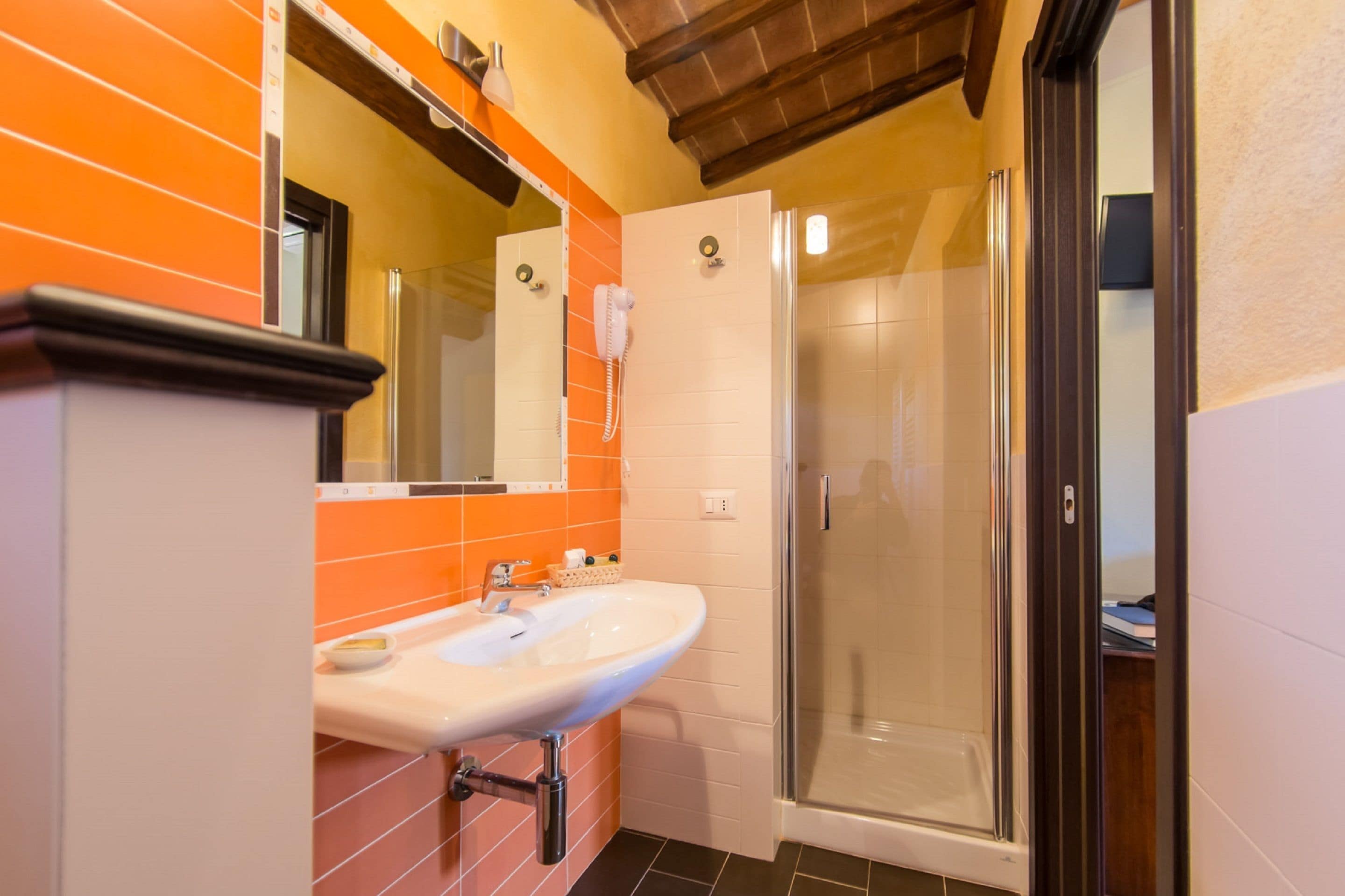 A bathroom with a white sink, orange tiles, a glass shower enclosure, and a wooden ceiling.