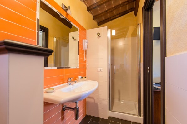 Un baño con un lavamanos blanco, baldosas anaranjadas, cabina de ducha de vidrio y techo de madera.