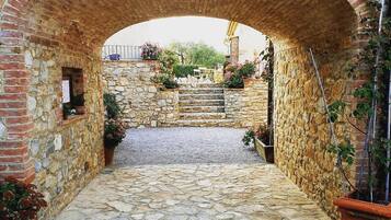 Un'entrata ad arco in pietra con un vialetto sterrato che vi conduce, circondata da mura in pietra e piante in vaso.