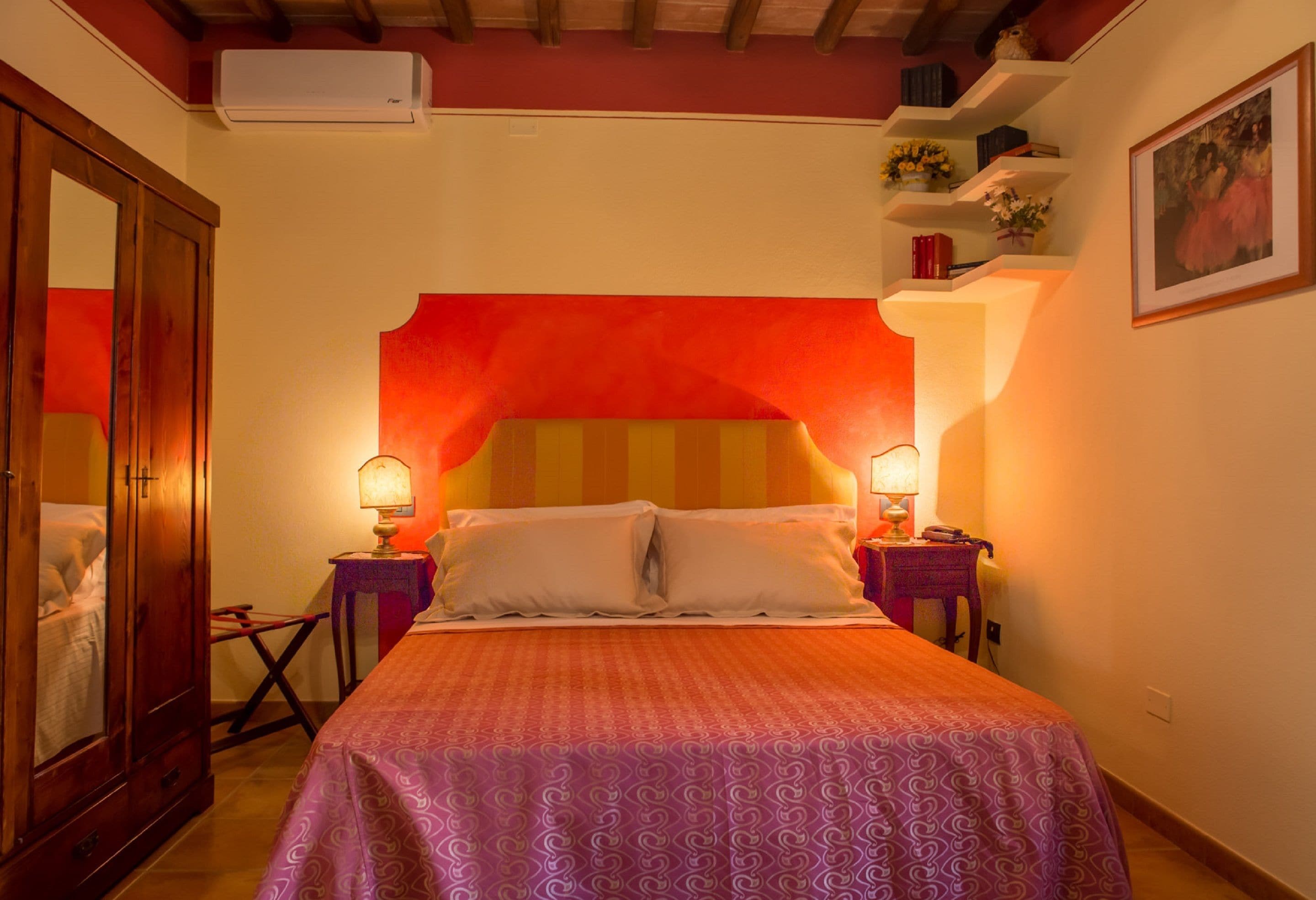 A bedroom with a large bed, two bedside tables with lamps, a wardrobe, and a shelf with decorative items.