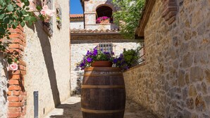 A narrow stone alley with a wooden barrel planter filled with purple flowers.