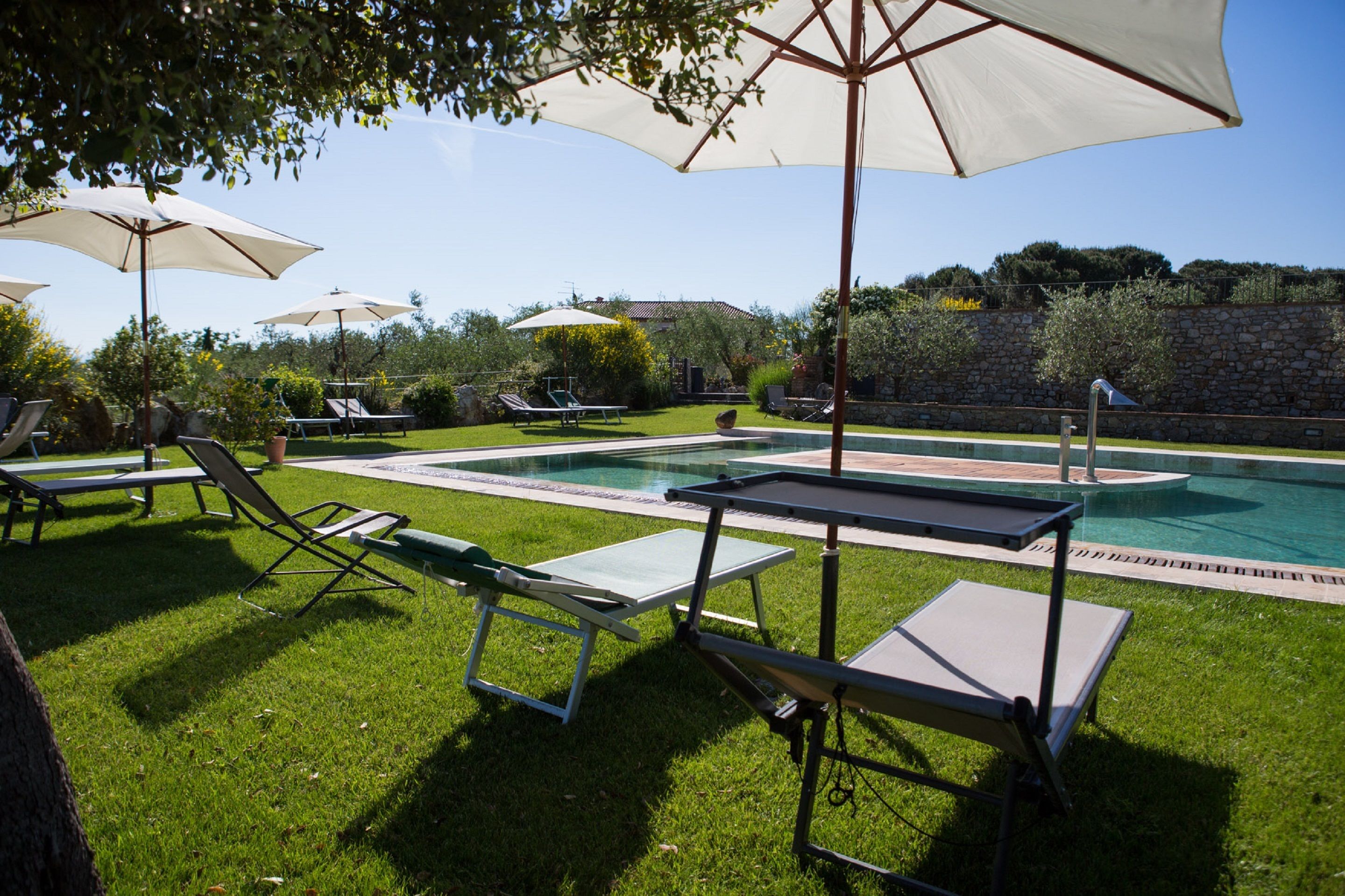 A poolside area with lounge chairs and umbrellas, a stone wall, and a clear sky.