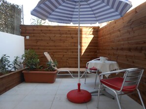Un patio con una mesa, sillas, una sombrilla y plantas en macetas.