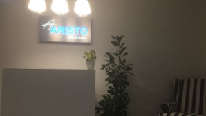 A reception area with a sign reading "ARISTO Apis & Suites," a reception desk, a potted plant, and a striped armchair. - Aristo (Hersonissos)