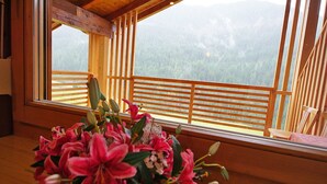 Een kamer met een houten balkon, een groot raam en een bloemenvaas.