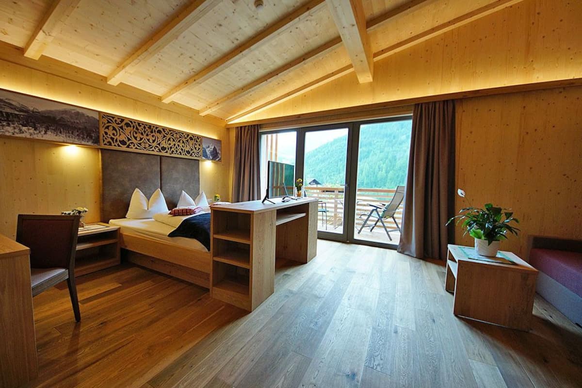 Ein Holzhäuschen im Inneren mit Bett, Schreibtisch, Stuhl und einem Balkon mit Bergblick.