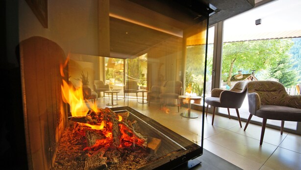 Een moderne woonkamer met een glazen haard, comfortabele zitplaatsen en uitzicht op het omliggende landschap.